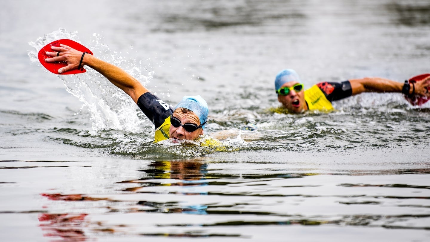 Two swimrun racers in full swim with red paddles, swim caps and race vests