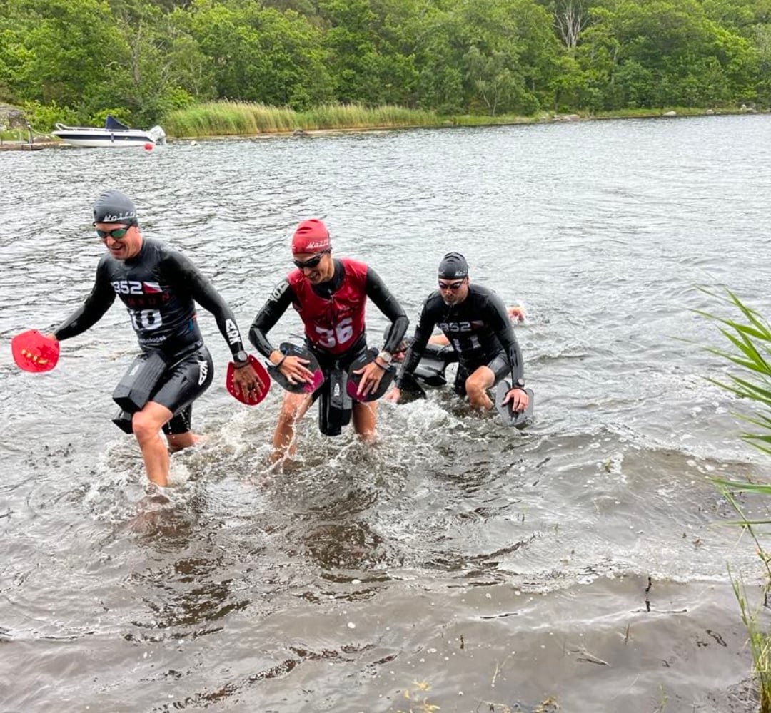 Tre swimrunåkare i tävlingsvästar på Dragsös strand
