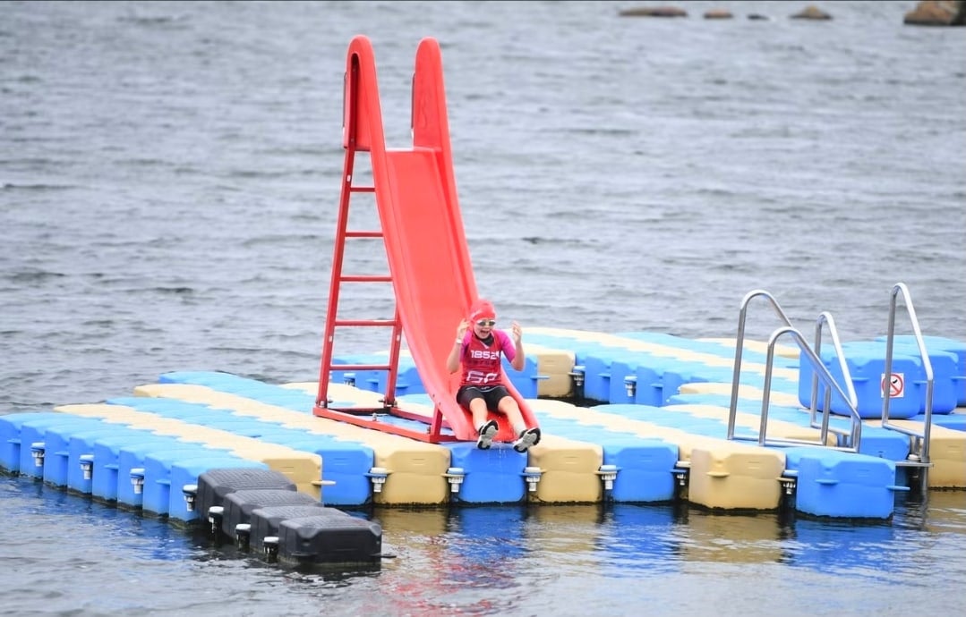 Deltagare åker ner för den röda rutschkanan på badflotten