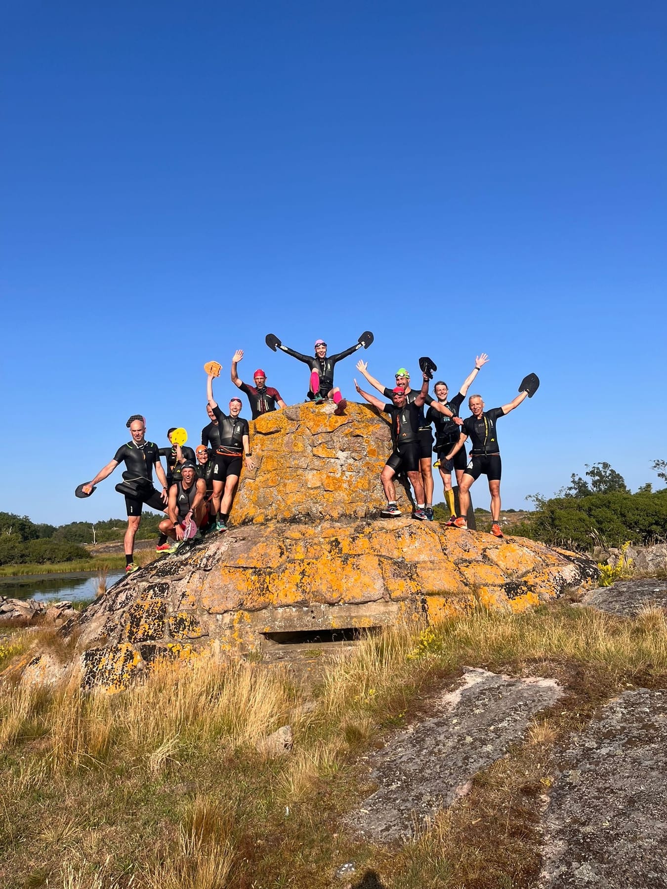 Group of swimrun racers with paddles raised on a lichen-covered rock.