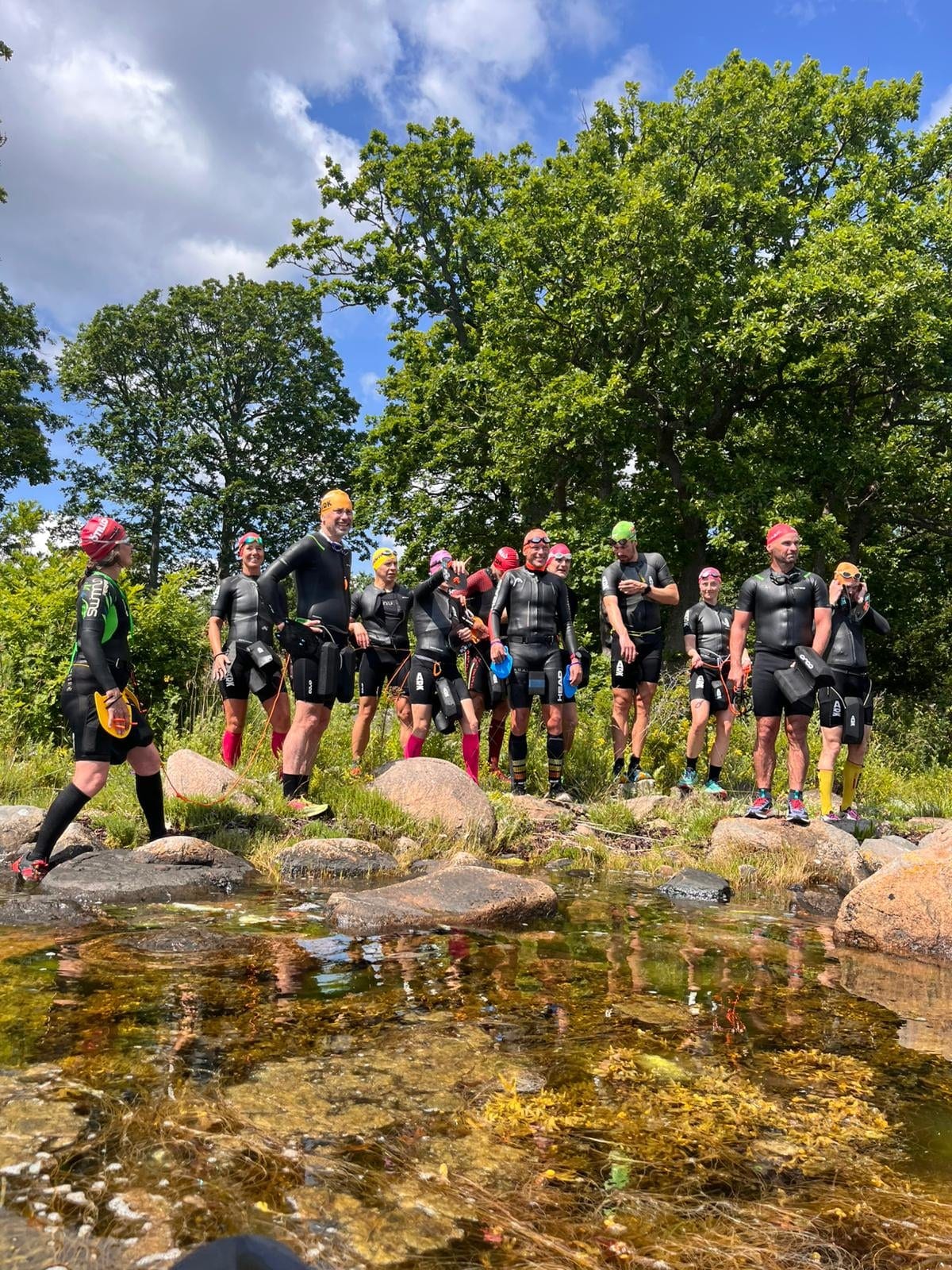 Swimrun-grupp i tävlingsdräkter på klippa vid stilla vatten